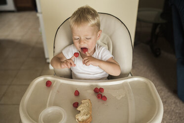 High angle view of baby boy eating raspberries while sitting on high-chair at home - CAVF56556