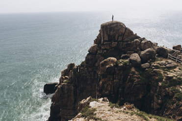 Blick aus mittlerer Entfernung auf einen Wanderer, der auf einer Klippe am Meer steht - CAVF56566