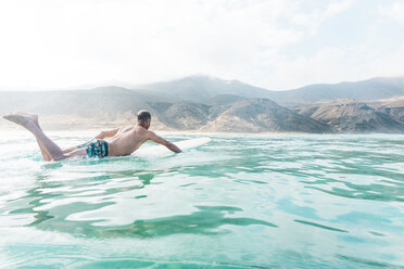 Full length of shirtless man surfing in sea against mountains - CAVF56574