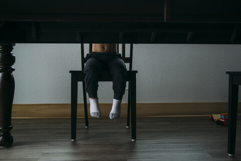 Niedriger Ausschnitt eines Jungen, der zu Hause auf einem Stuhl am Tisch sitzt, lizenzfreies Stockfoto