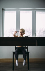 Shirtless boy eating while sitting on chair by window at home - CAVF56616