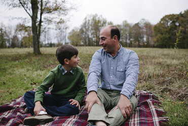 Vater mit Sohn auf einer Decke sitzend gegen den Himmel im Park - CAVF56622