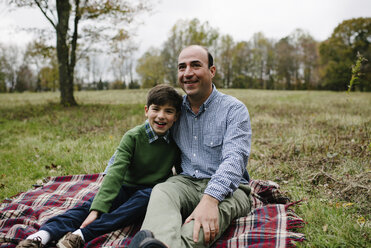 Porträt eines Vaters mit Sohn auf einer Decke sitzend gegen den Himmel im Park - CAVF56623