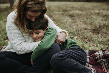 Glückliche Mutter, die ihren Sohn umarmt, während sie auf einer Decke im Park sitzt - CAVF56624