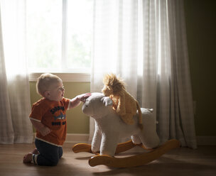 Baby-Junge spielt mit Lamm Wippe, während kniend auf dem Boden zu Hause - CAVF56629