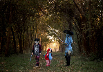 Geschwister tragen Halloween-Kostüme, während sie im Park an Bäumen stehen - CAVF56630