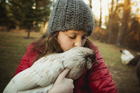 Mädchen küsst Huhn, während sie in einer Geflügelfarm steht, lizenzfreies Stockfoto