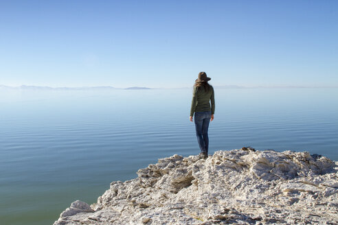 Rückansicht einer Frau, die auf einem Felsen auf der Antelope Island steht, vor einem klaren blauen Himmel - CAVF56640