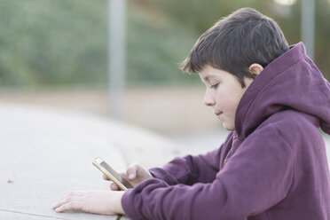Side view of boy using mobile phone while sitting outdoors - CAVF56656