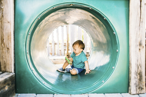 Baby in voller Länge in der Röhre sitzend auf dem Spielplatz, lizenzfreies Stockfoto