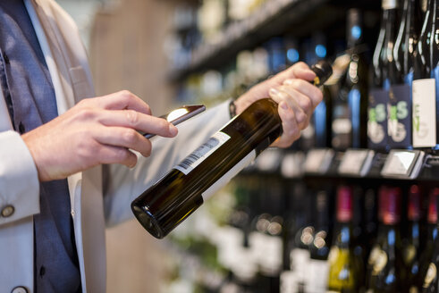 Mature man choosing wine in supermarket, scanning product information ith his smartphone - DIGF05492