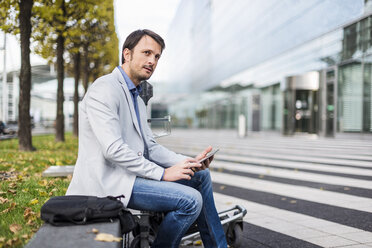 Businessman sitting on a bench, using digital tablet - DIGF05501