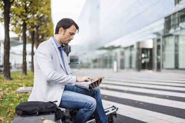 Businessman sitting on a bench, using digital tablet - DIGF05502