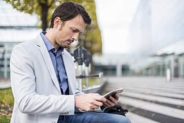 Geschäftsmann, der auf einer Bank sitzt und ein digitales Tablet benutzt - DIGF05503