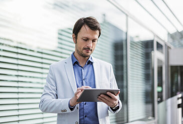 Businessman sitting on a bench, using digital tablet - DIGF05504