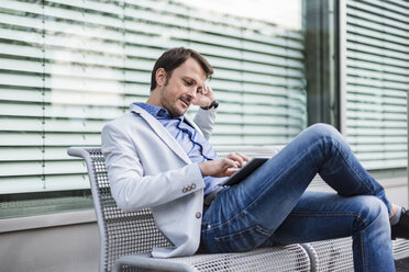 Geschäftsmann, der auf einer Bank sitzt und ein digitales Tablet benutzt - DIGF05506
