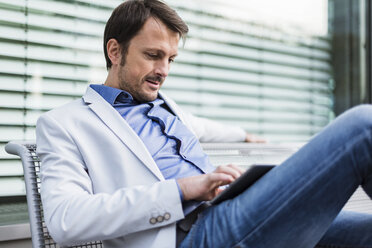Geschäftsmann, der auf einer Bank sitzt und ein digitales Tablet benutzt - DIGF05507