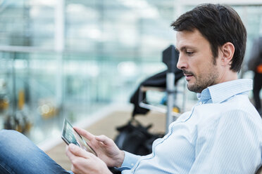 Businessman waiting in airport departure area, using digital tablet - DIGF05526