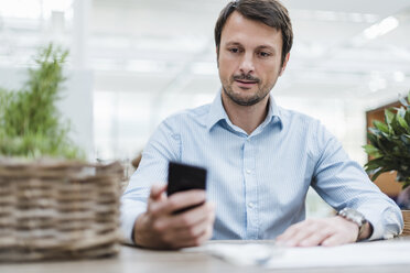 Businessman working in office, using smartphone - DIGF05535