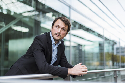 Geschäftsmann, der am Flughafen wartet und sich auf das Geländer stützt, lizenzfreies Stockfoto