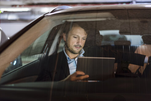 Geschäftsmann sitzt nachts im Auto und benutzt ein digitales Tablet - DIGF05555