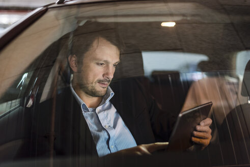 Geschäftsmann sitzt nachts im Auto und benutzt ein digitales Tablet - DIGF05556