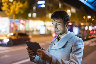 Businessman with digital tablet standing at a bus stop at night - DIGF05560