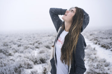 Frau mit langen Haaren, die auf einem schneebedeckten Feld steht und nach oben schaut - CAVF56669