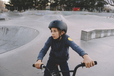 Boy wearing helmet while sitting on bicycle at skateboard park - CAVF56676