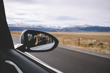 Reflection of woman photographing seen in side-view mirror against mountains and cloudy sky - CAVF56677