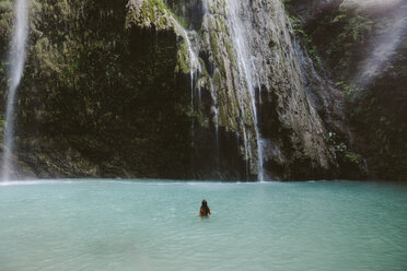 Rückansicht einer im Fluss schwimmenden Frau bei einem Wasserfall im Wald - CAVF56686