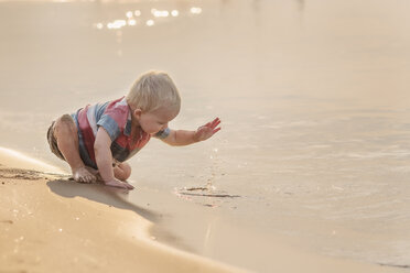 Baby boy playing with water while sitting at beach - CAVF56689