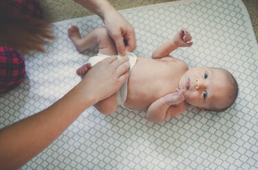Abgeschnittenes Bild von Mutter trägt Windel für Baby-Junge auf Decke liegen - CAVF56702