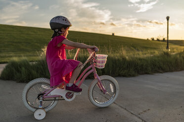 Seitenansicht eines Mädchens, das auf der Straße Fahrrad fahren lernt, gegen den Himmel - CAVF56708