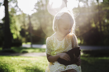 Cute girl petting kitten while sitting at park during sunny day - CAVF56727
