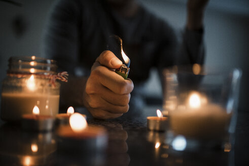 Mittelteil eines Mannes, der mit einem Feuerzeug auf einem Tisch in einer Dunkelkammer Kerzen anzündet - CAVF56731