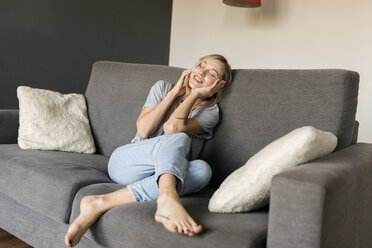 Lächelnde junge Frau mit geschlossenen Augen auf der Couch sitzend und mit dem Handy telefonierend - VABF01851