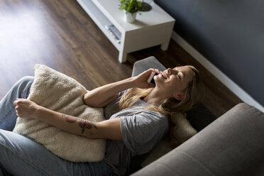 Lächelnde junge Frau mit geschlossenen Augen auf der Couch liegend und mit dem Handy telefonierend - VABF01860