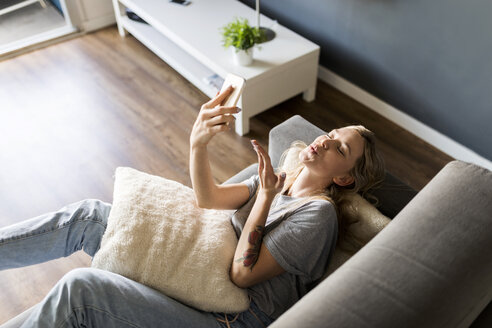 Lächelnde junge Frau liegt auf der Couch und macht ein Selfie - VABF01861