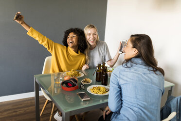 Glückliche Freundinnen sitzen am Esstisch und machen ein Selfie - VABF01869