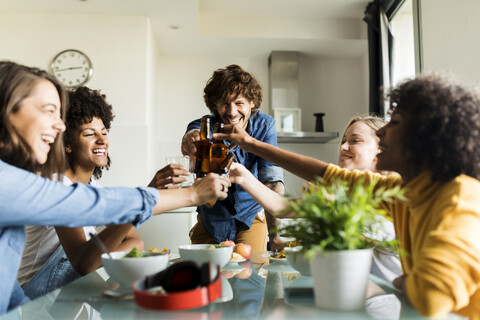 Cheerful friends clinking beer bottles at dining table stock photo