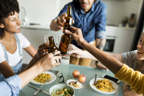 Fröhliche Freunde stoßen am Esstisch mit Bierflaschen an - VABF01885