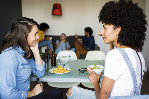 Freundinnen sitzen am Esstisch mit Freunden im Hintergrund, lizenzfreies Stockfoto