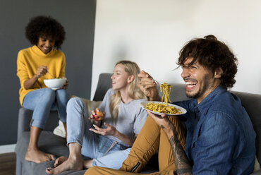 Fröhliche Freunde sitzen auf der Couch, reden und essen - VABF01887