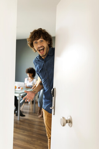 Porträt eines überraschten Mannes mit Freunden im Hintergrund, die die Tür öffnen, lizenzfreies Stockfoto