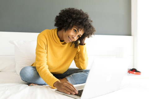 Smiling woman sitting on bed using laptop stock photo