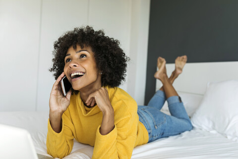 Glückliche Frau liegt auf dem Bett und spricht mit ihrem Handy, lizenzfreies Stockfoto