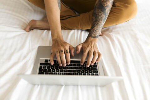 Nahaufnahme eines tätowierten Mannes mit Laptop im Bett, lizenzfreies Stockfoto