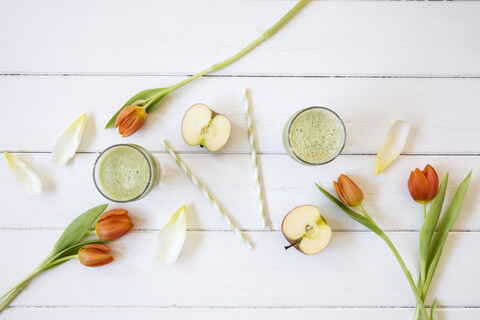 Zwei Gläser mit grünem Smoothie, geschnittenem Apfel, Chicorée und Tulpen auf weißem Grund, lizenzfreies Stockfoto