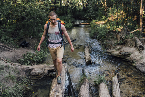 Junger Mann mit Rucksack balanciert auf Totholz in einem Wald, lizenzfreies Stockfoto